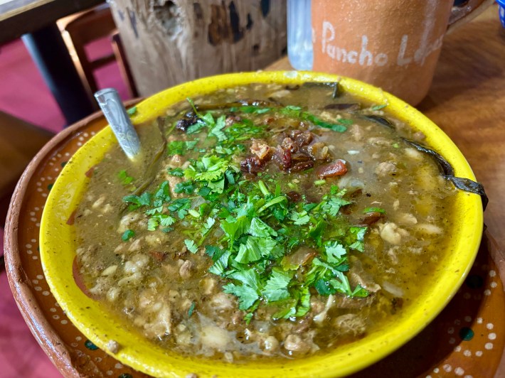 a bowl of soup with meat, green broth, and fresh cilantro