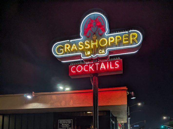a glowing neon sign outside of a bar reading "Grasshopper LB CA Cocktails"
