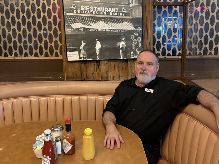 an older man sits in a curved booth at a restaurant