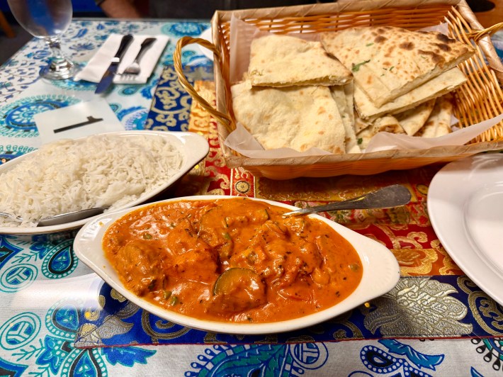 a basket of naan, a serving dish of butter chicken, and rice on a vibrant tablecloth