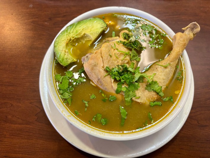a bowl of green soup with chicken, avocado, and cilantro