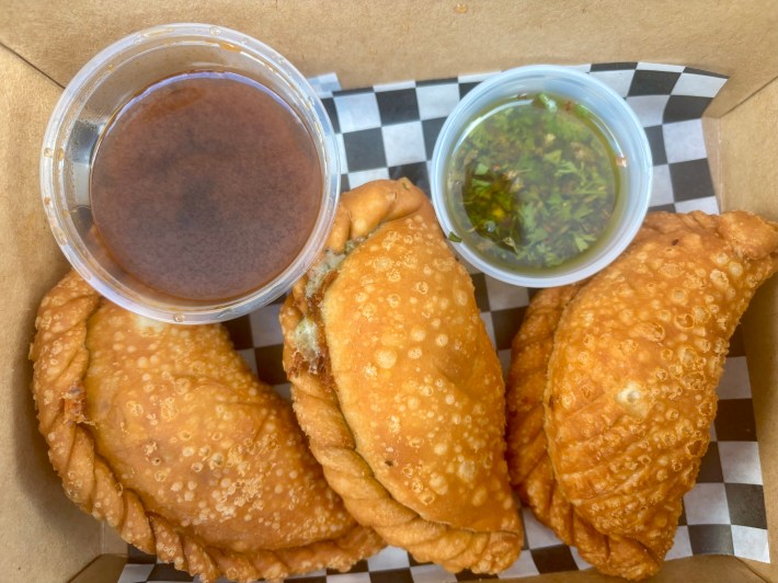 three empanadas in a cardboard take-away box with two sauces on the side