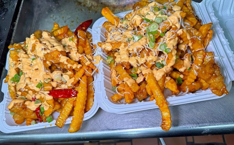 two to-go boxes of crnkle fries covered in cheese and green onions