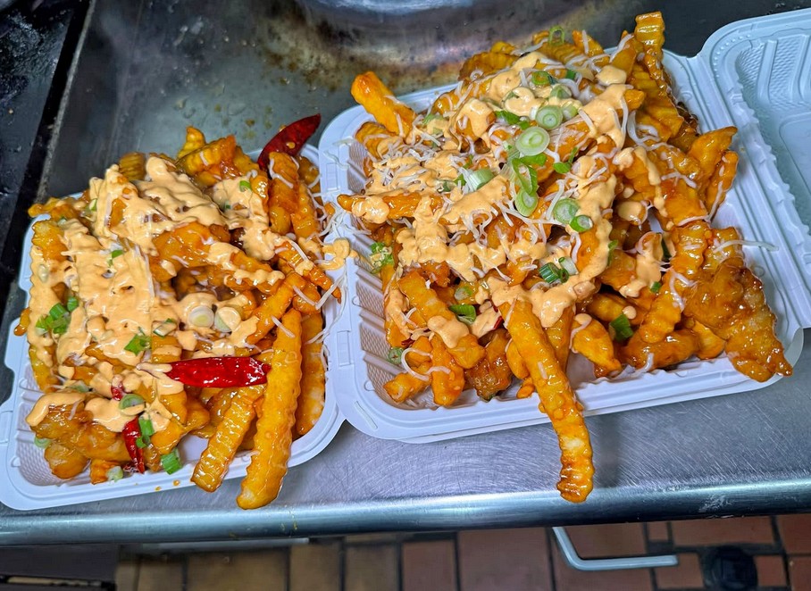 two to-go boxes of crnkle fries covered in cheese and green onions
