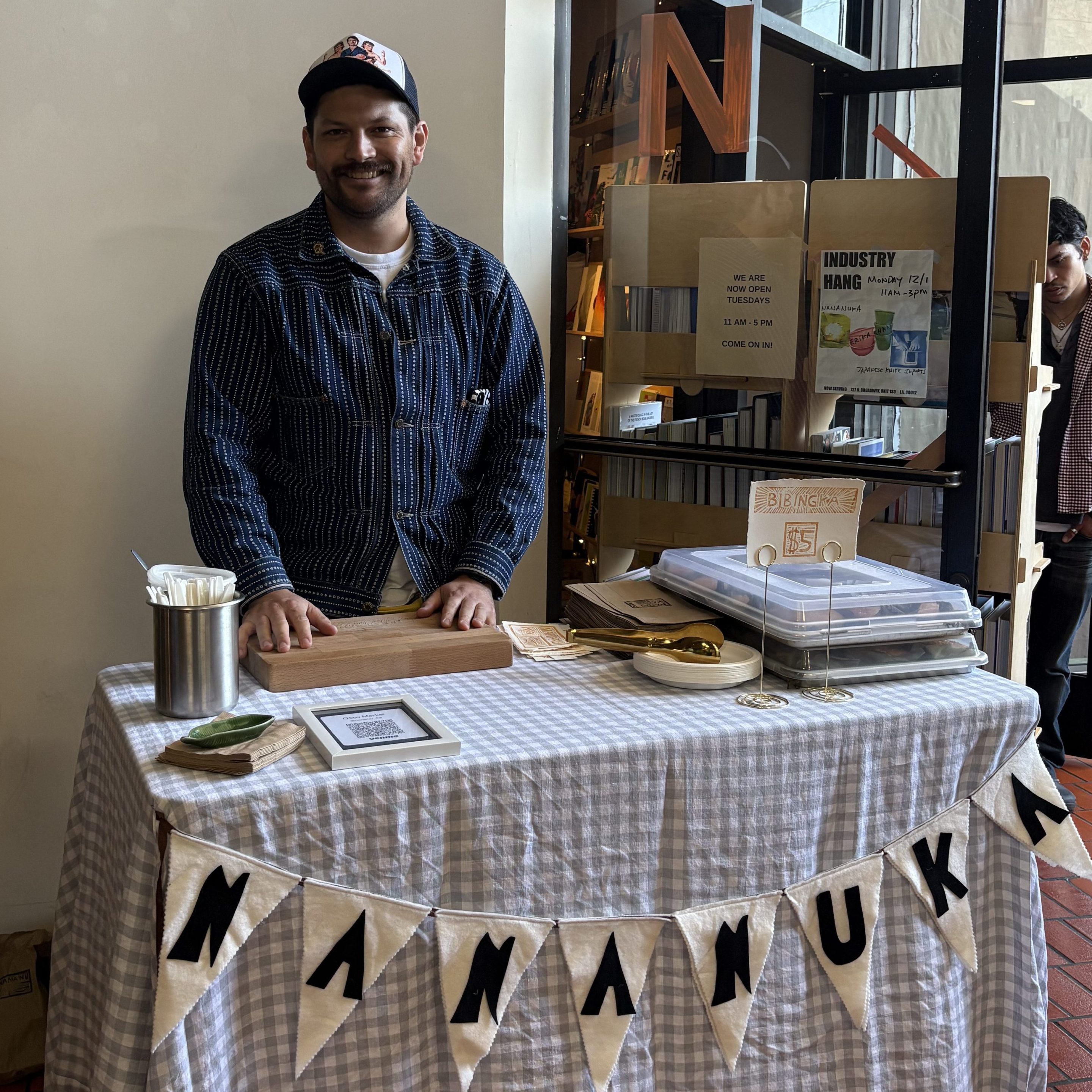 a man smiles at a table labeled "NANANUKA"