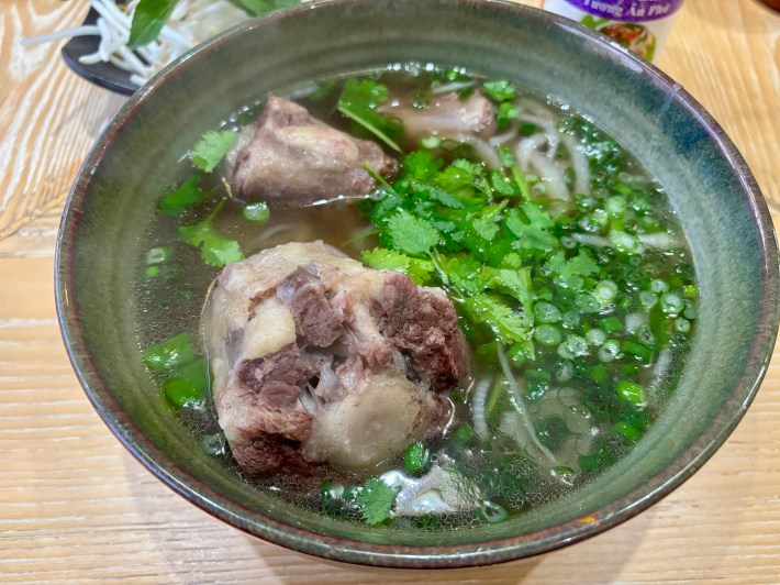 a ceramic blue bowl full of oxtail pho with onions and cilantro