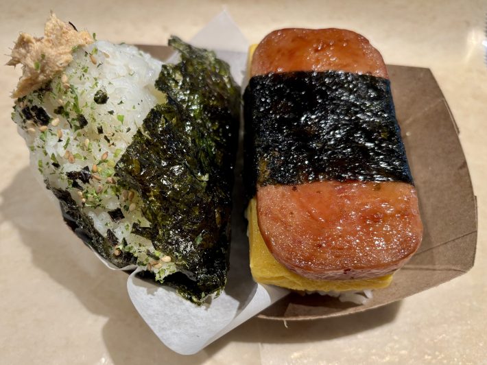 a spicy tuna onigiri and spam-egg musubi on a small cardboard plate