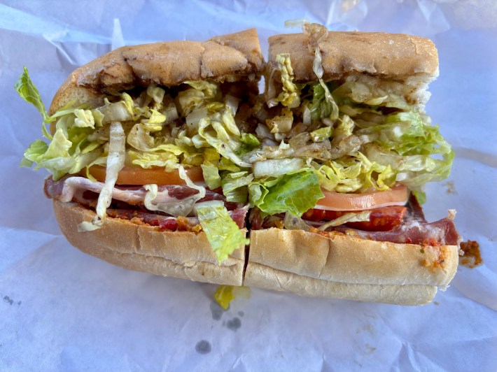 a sandwich cut in half and packed with Hot Sopressata, Hot Capicolla, Pepperoni, and Provolone, with romaine, sliced tomatoes and spicy cherry pepper pesto