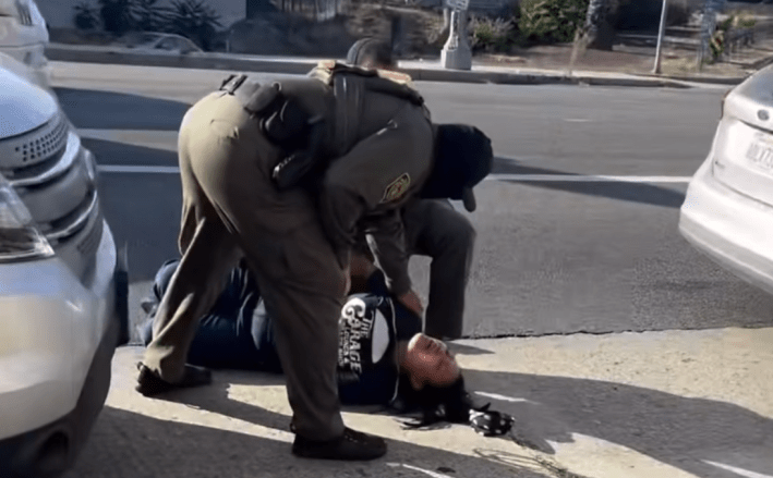 an armed officer hovers over a woman pinned to the ground