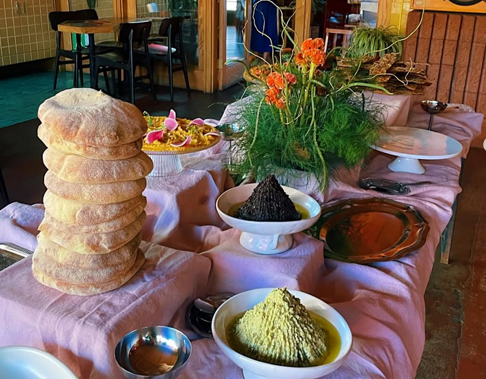 A table set with Moroccan dishes in white bowls, next to a vase of orange flowers