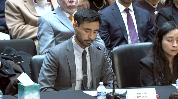 a man in a suit sits in front of a microphone at a court hearing