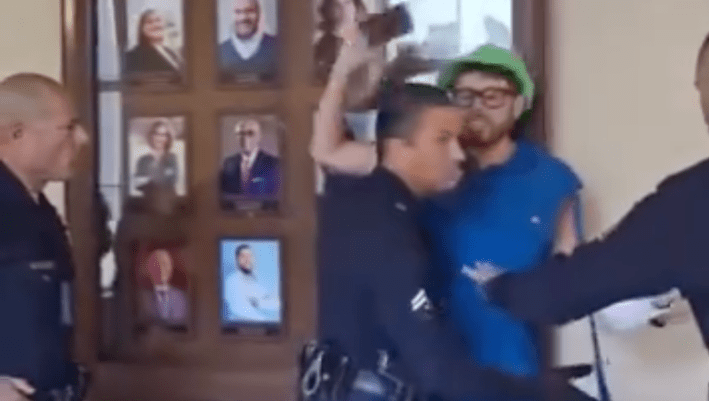 a man protesting and recording is escorted away by officers