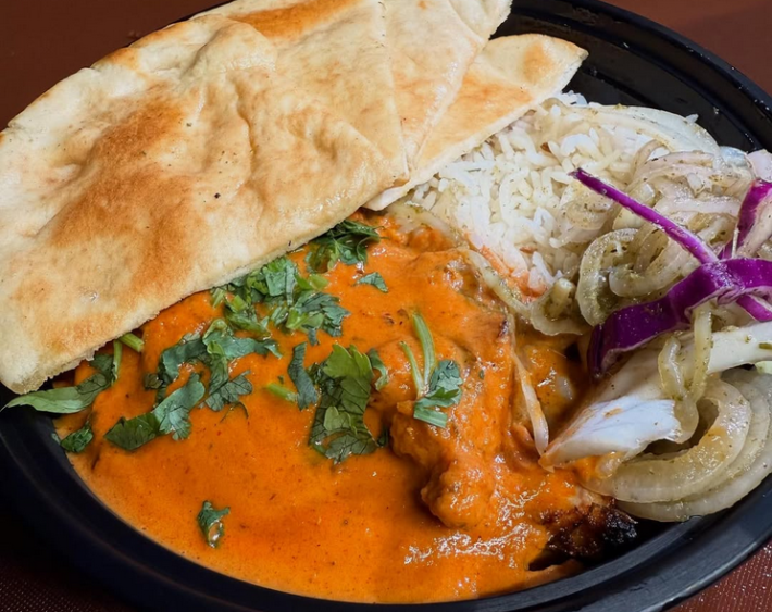 A plate of butter chicken halfcovered with naan and with basmati rice on the side
