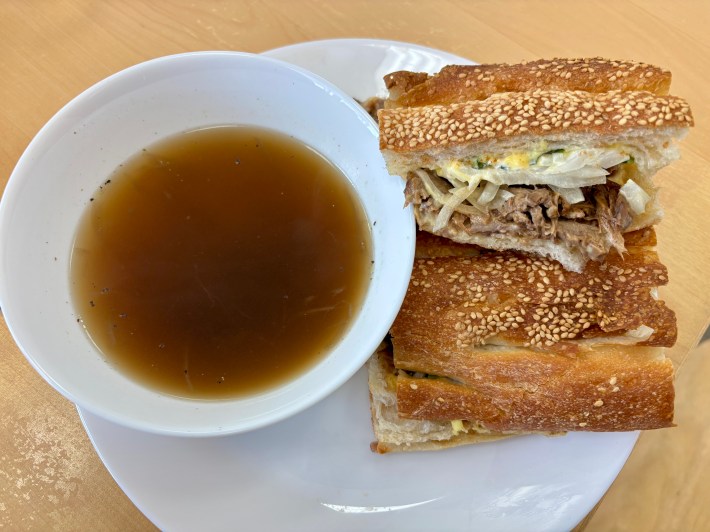 a bowl with a broth for dipping next to a sandwich cut into two