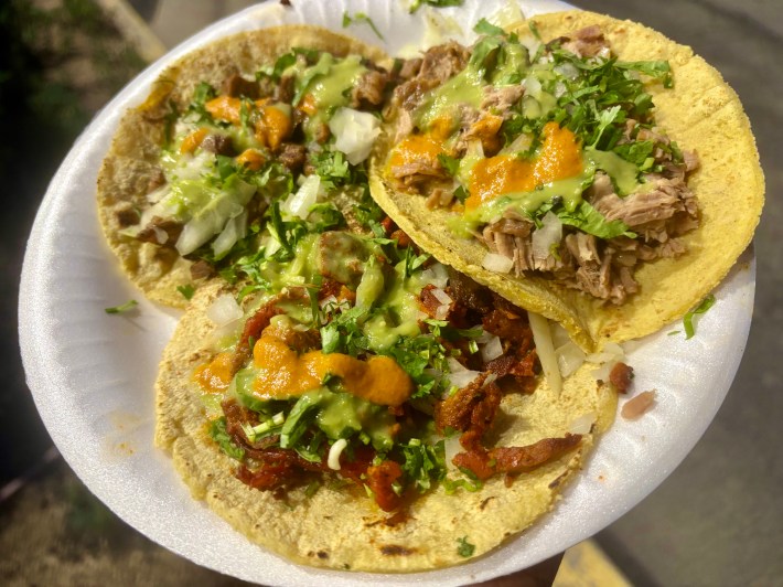 a plate of three different tacos on corn tortillas with onions, cilantro, and salsa