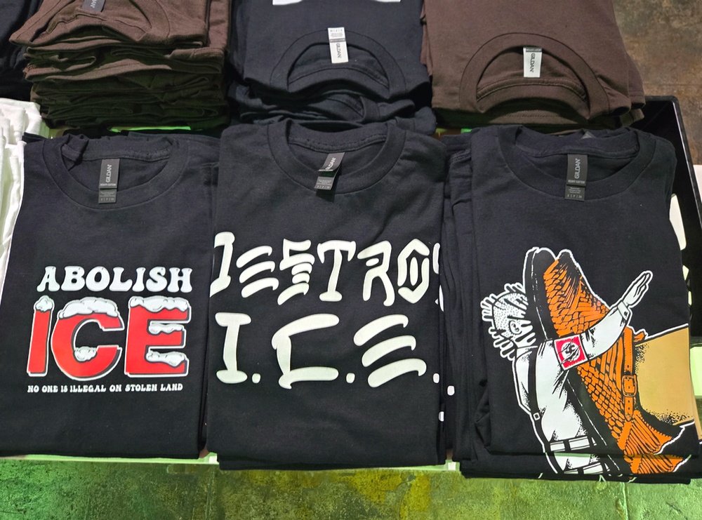 Three black anti-ICE t-shirts side-by-side on a store's table.