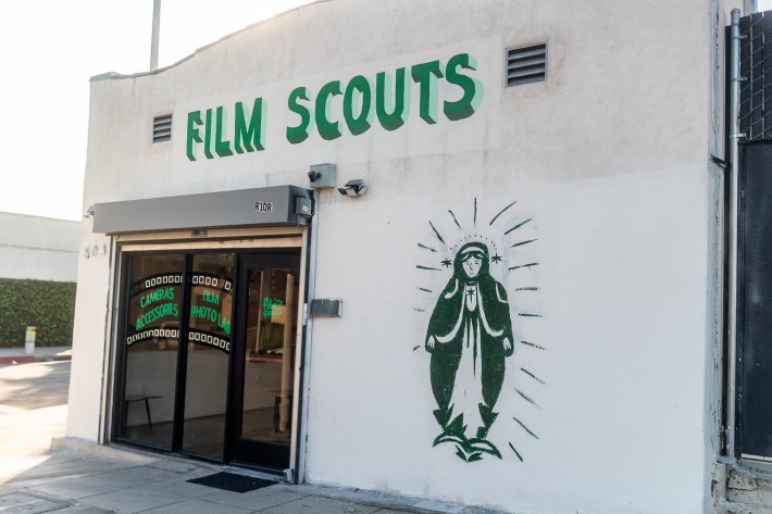 The exterior of a film shop called "film scouts." the lettering is in a bold green, and there is a mural of La Reina in a similar green color