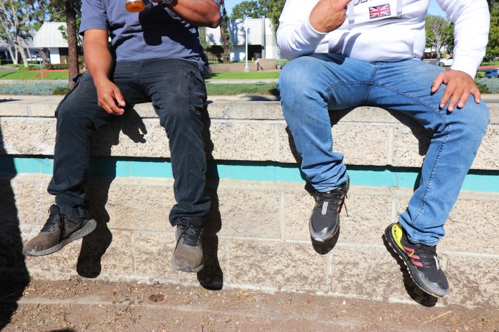 Two men, their faces out of frame, sit on a ledge outside