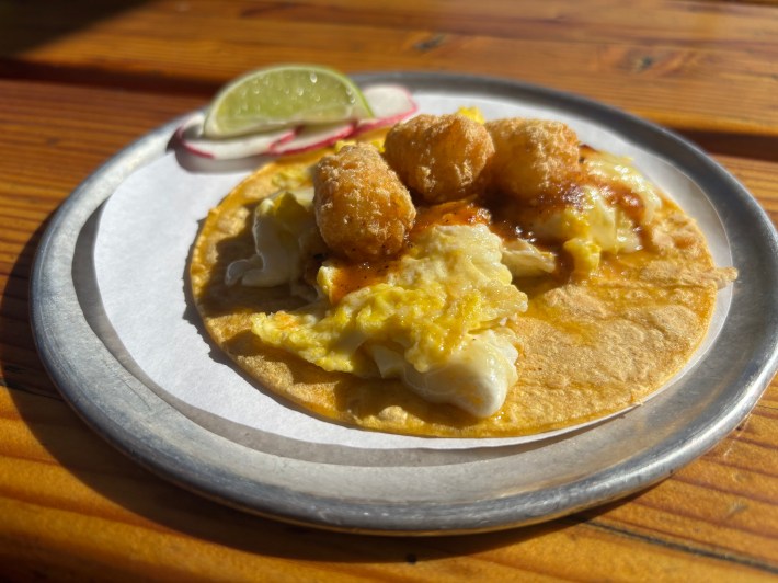 a silver plate with a corn tortilla, scrambled eggs, and tater tots
