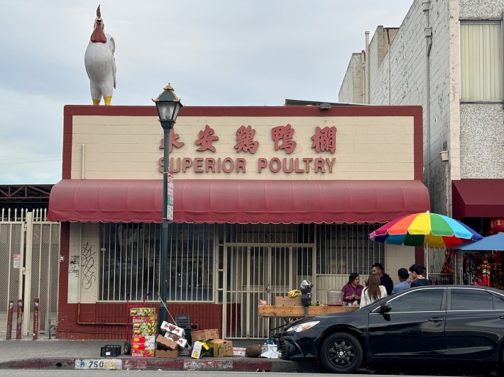 the exterior of a live poultry store. a large rooster is on top.