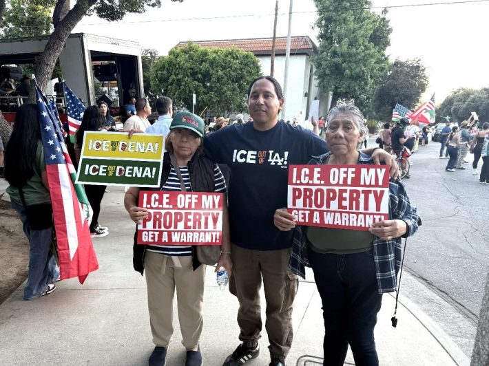 two older women hold protest signs. a man also poses between them