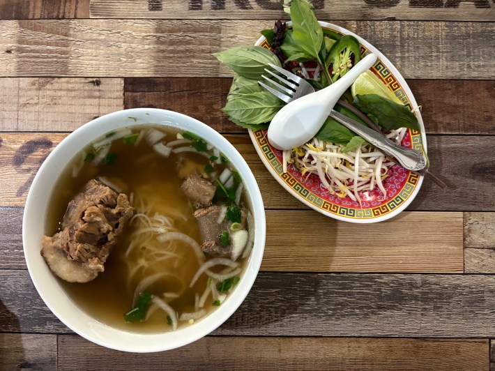 a bowl of oxtail pho and a plate of herbs and beansprouts