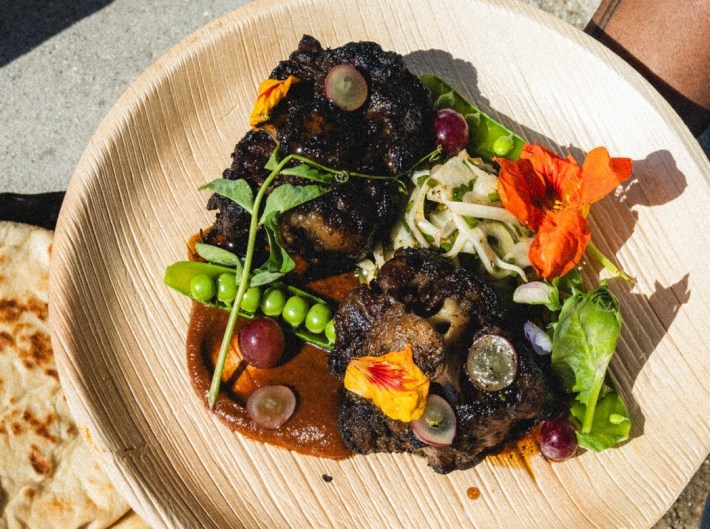 a PLATE OF JERK CHICKEN WITH PEAS, SAUCE MOYO, AND EDIBLE FLOWERS