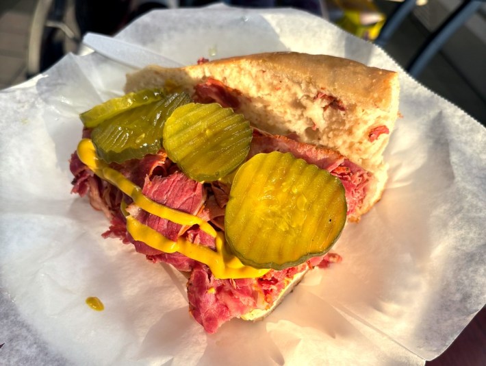 a piece of sub bread with pastrami, mustard, and pickles on it