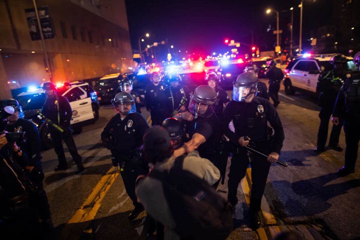 Polie with batons in face shields grab a protestor by the neck