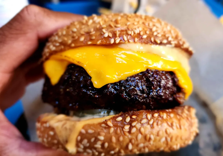 A big cheeseburger on a sesame bun being held by a hand