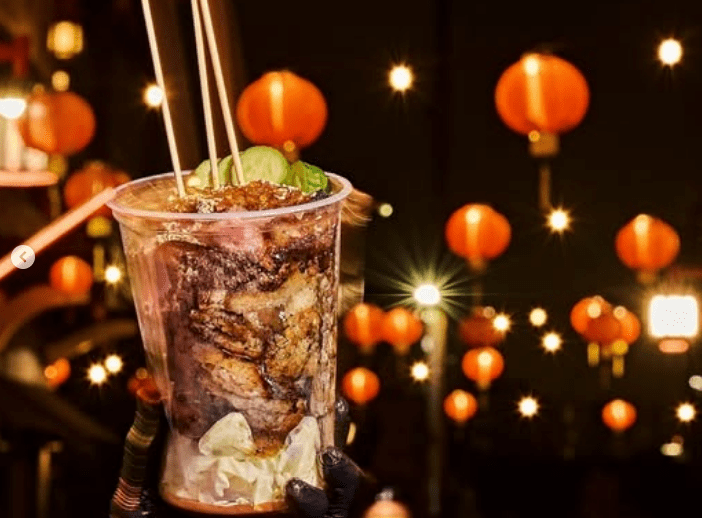 A cup filled with barbecued meats with chopsticks sticking out and red paper lanterns in back