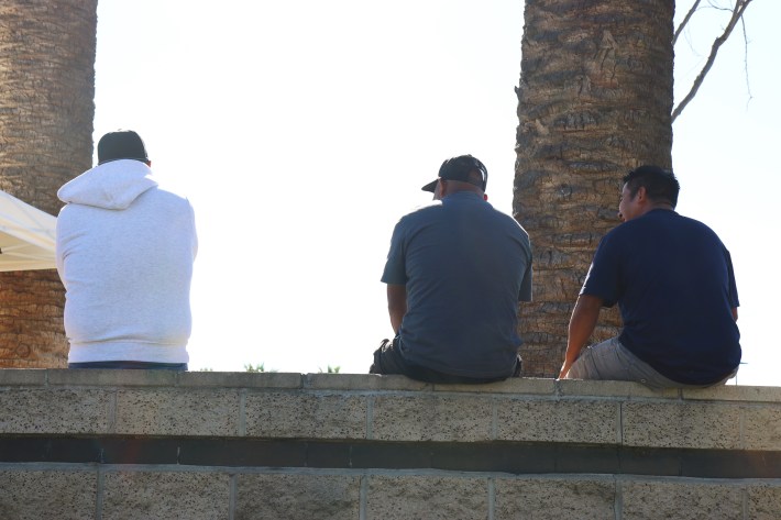 three men sit outside on a ledge