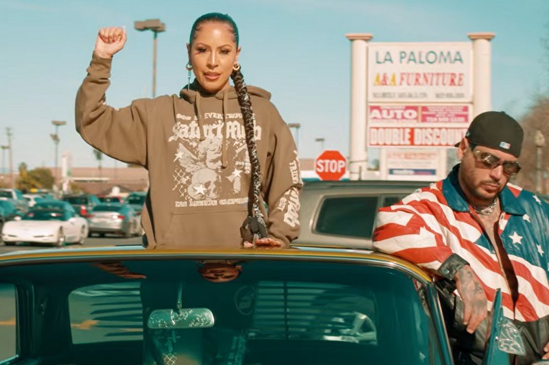 A woman holds a fist in the air while popping out of a sunroof next to a man with a U.S. flag jacket.