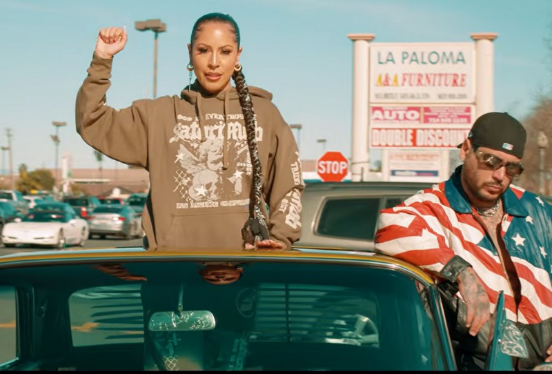A woman holds a fist in the air while popping out of a sunroof next to a man with a U.S. flag jacket.