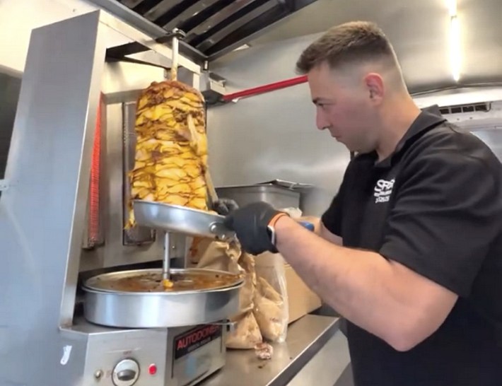A man slicing chicken shawarma in a food truck