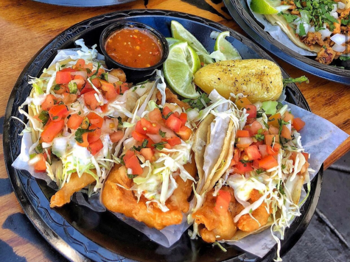 Taco Nazo's famous fish tacos served on a plate with red salsa and a Anaheim chile.