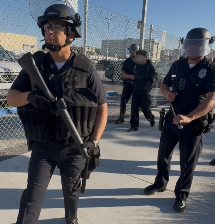 two officers armed in the foreground. a boy being arrested in the background