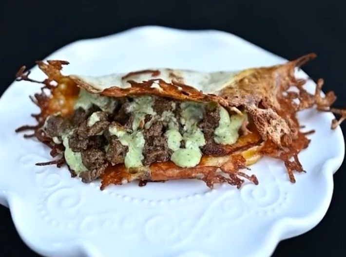 A cheese-crusted filet mignon taco on a white plate, with green crema leaking out the front