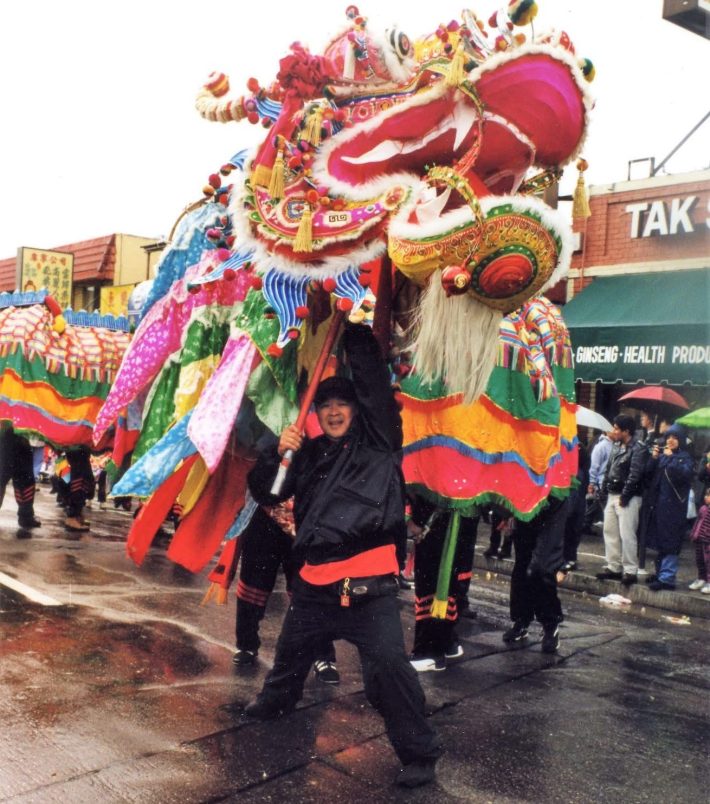 A man smiles and holds a costume dragon head above himself.
