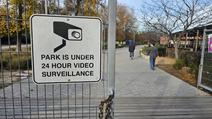 A sign attached to a gate reads: "park is under 24 hour video surveillance."