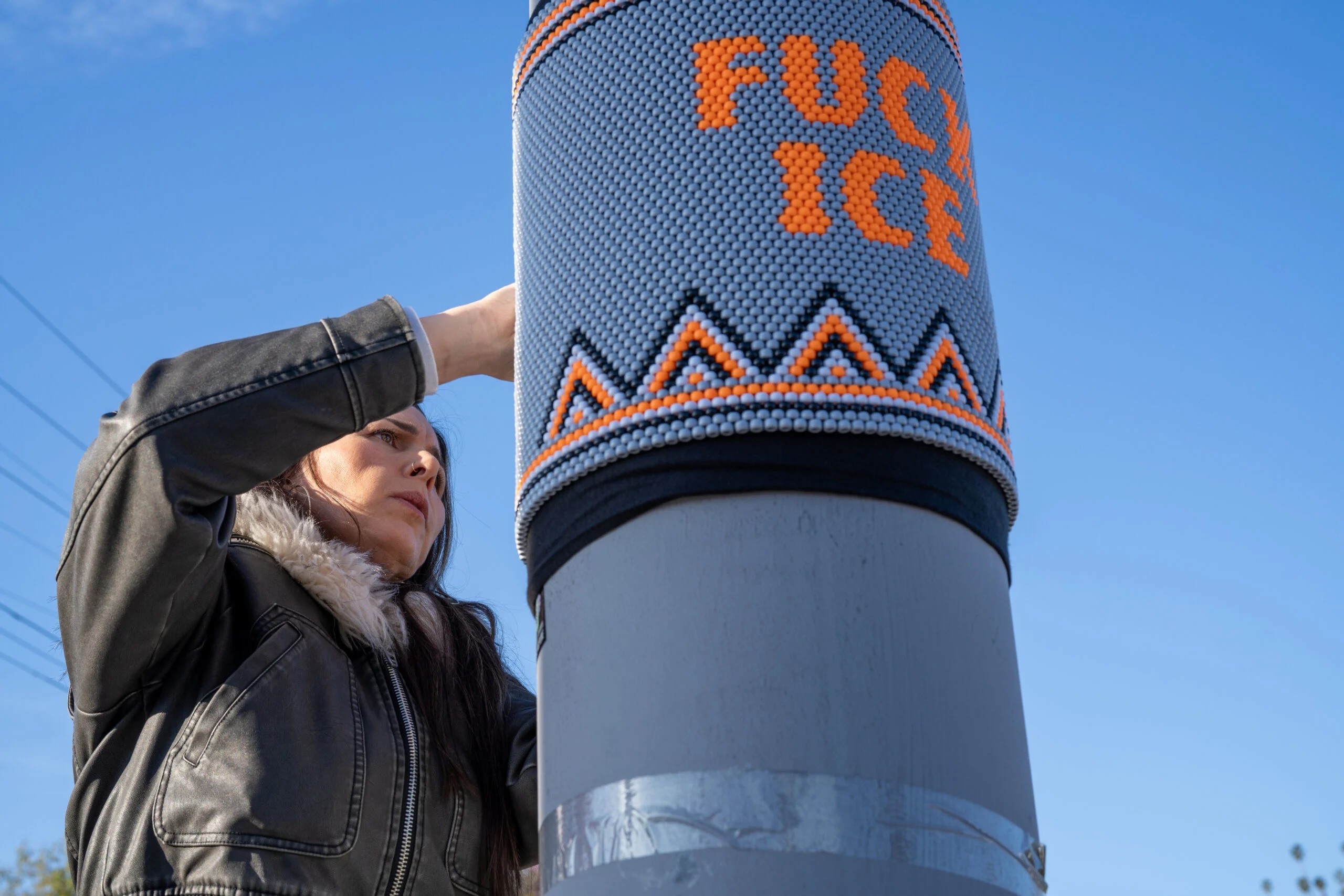 a woman fixes bead art to a street pole