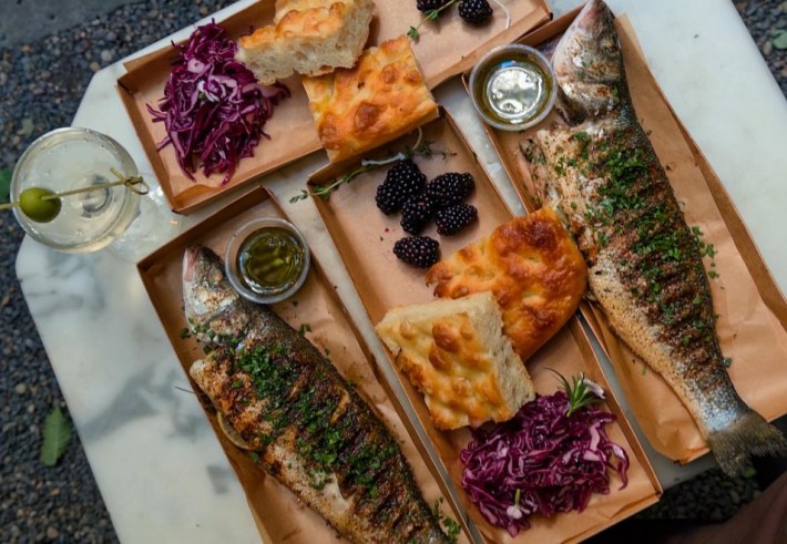 A spread with a martini, foccacia, blackberries and two whole branzino