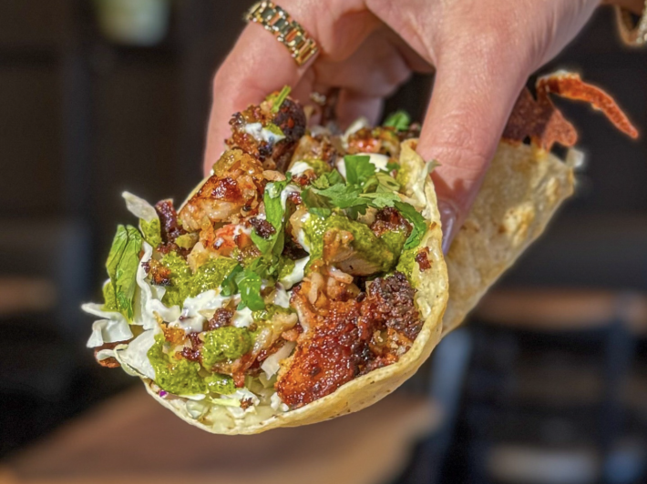 A taco revolcado from El Coraloense is filled with marinated mahi mahi al pastor that is grilled to perfection and served with a side of fresh cabbage, taco cream, and zesty green sauce for the perfect balance of flavor.