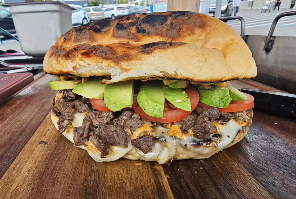 A giant torta al carbon with asada, avocado, cheese, and tomato