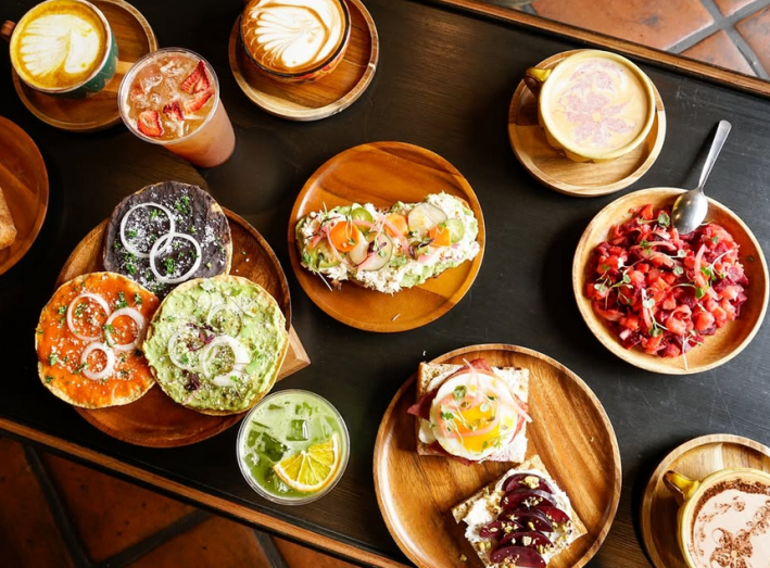 Egg dishes, tostadas, and spread toasts and lattes on a table at Ülëw Coffee & Juice.