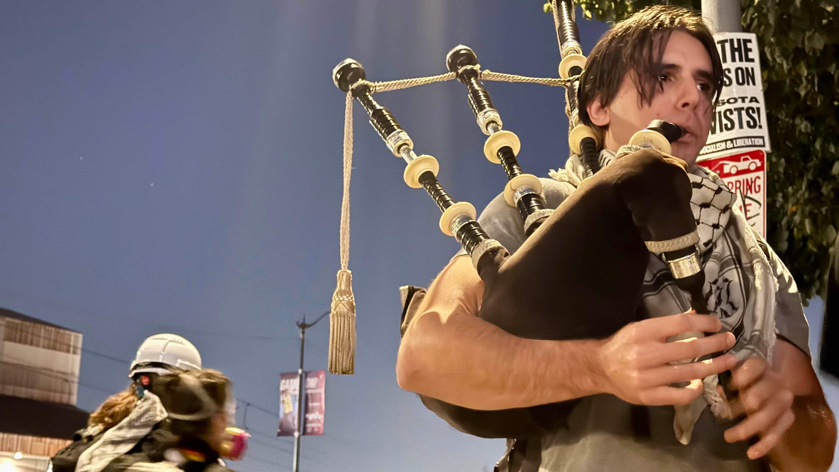 a young man wearing a keffiyeh plays the bagpipes