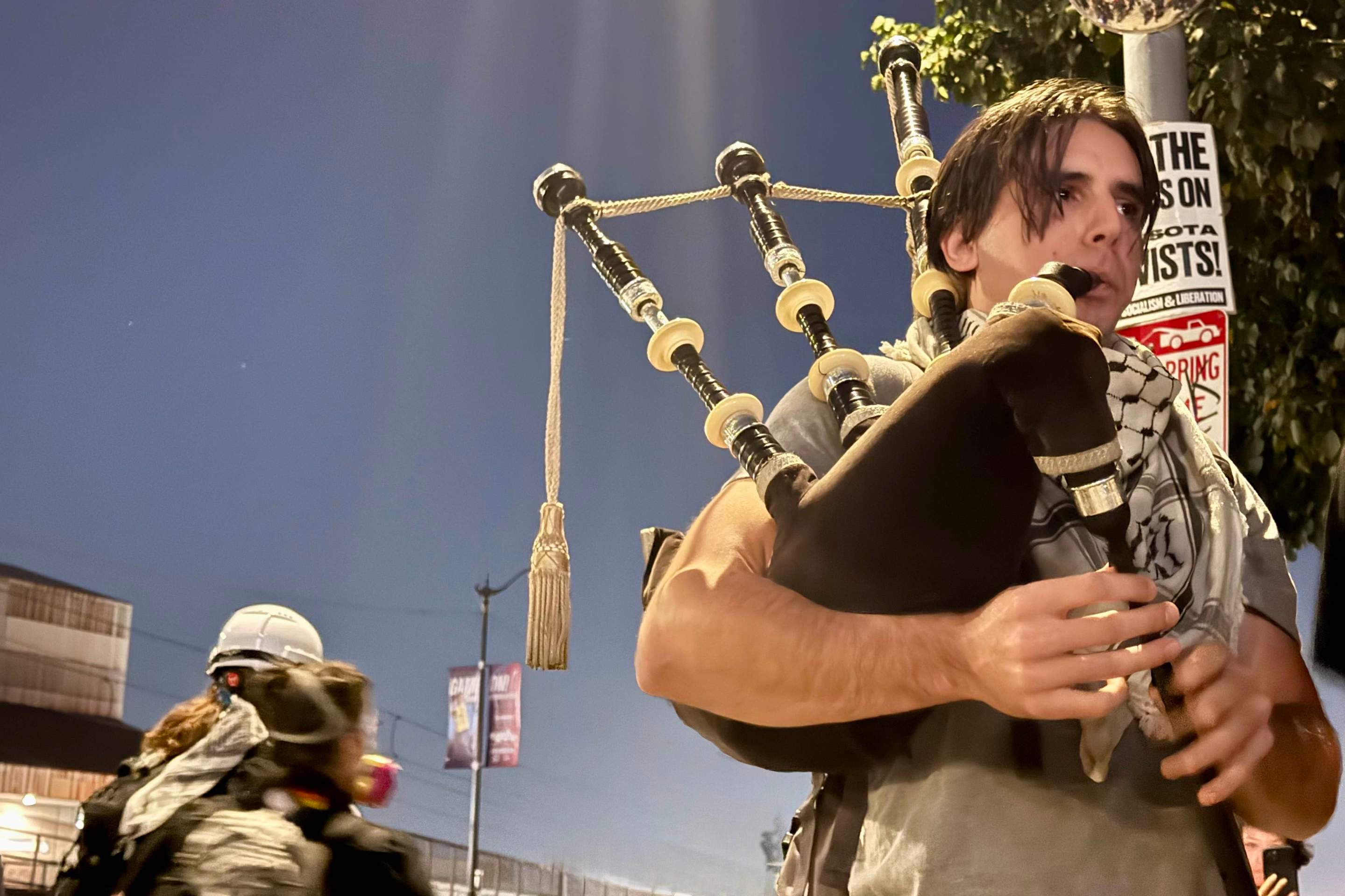 a young man wearing a keffiyeh plays the bagpipes