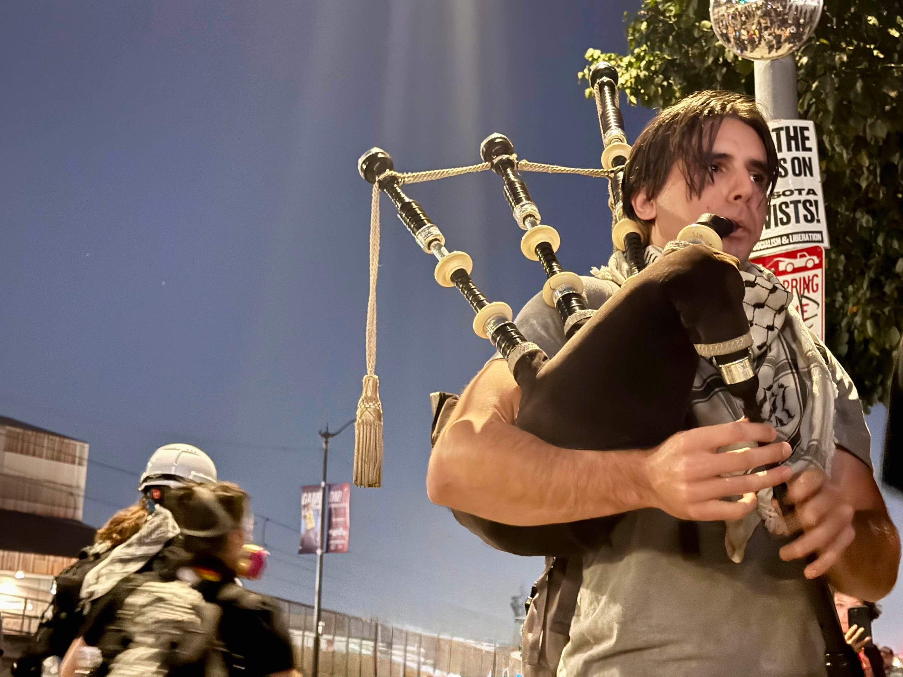 a young man wearing a keffiyeh plays the bagpipes