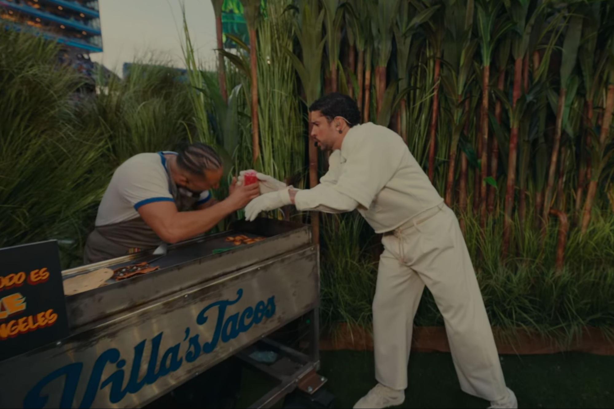 a man behind a taco stand hands a drink to a man in an all-white outfit