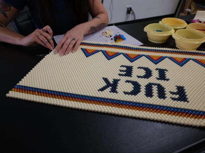 a woman creates bead art that reads "FUCK ICE"